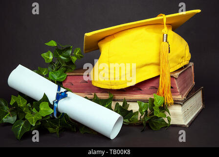 Oro brillante tappo di graduazione sui vecchi libri con il bianco vuoto diploma legate con nastro blu Foto Stock