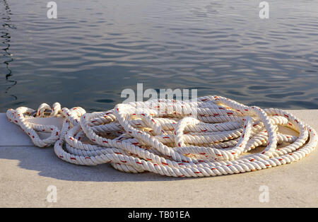 Pila di corda bianca per ormeggio barche o yacht sul dock di pietra in riva al mare Foto Stock