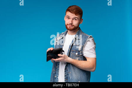 Triste uomo millenario che mostra il suo portafoglio vuoto alla fotocamera Foto Stock