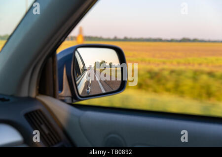 Guardando fuori dalla macchina e vista laterale specchio a terreni agricoli rurale durante la guida in autostrada in Sud America. Foto Stock