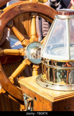 Un volante in legno ann vintage compass brillano alla luce del sole su una gita in barca a vela nel Maine. Foto Stock