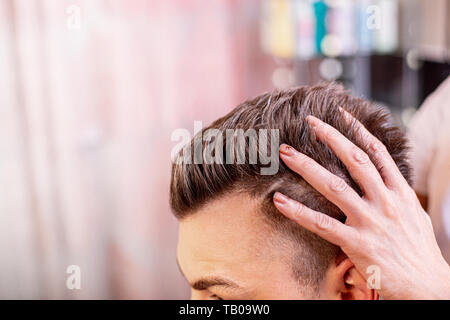 Il comandante mette i capelli di un uomo in un barbiere, un parrucchiere rende un'acconciatura per un giovane uomo con l aiuto di gel e vernice. Foto Stock