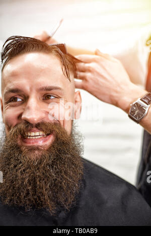 Master taglia i capelli e la barba di uomini del barbiere, parrucchiere rende l'acconciatura per un giovane uomo Foto Stock