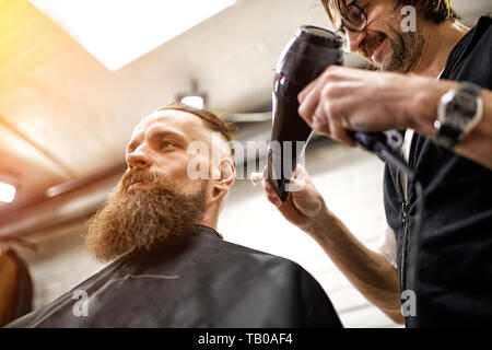 Master taglia i capelli e la barba di uomini del barbiere, parrucchiere rende l'acconciatura per un giovane uomo Foto Stock