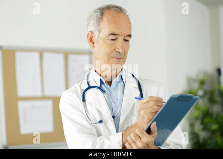 Senior medico uomo riempire la forma medica a clipboard Foto Stock