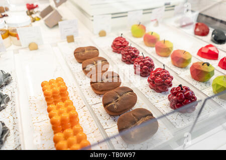 Righe multicolore di torte e dessert nella vetrina di un negozio di pasticceria. Mousse di moderno dessert, snack dolce. in forma di chicchi di caffè, ciliegie Foto Stock