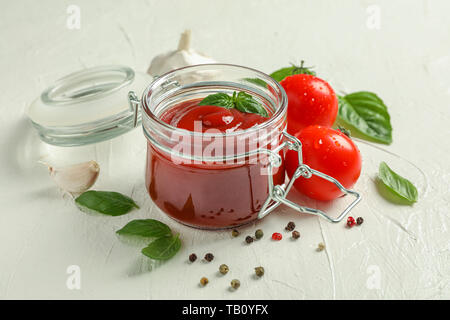 Composizione con pomodori freschi, basilico, peperoncino, aglio e la salsa in un barattolo di vetro su sfondo bianco, spazio per il testo Foto Stock