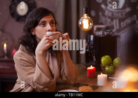 Ritratto di una giovane e bella donna che mantiene una tazza di caffè presso il bar in una caffetteria. Bella donna rilassante in un coffee shop con una tazza di caffè. Foto Stock