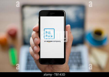 Un uomo guarda al suo iPhone che visualizza il logo PillPack (solo uso editoriale). Foto Stock