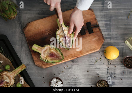 Donna preparando gustosi piatti di carciofi crudi sulla tabella grigia Foto Stock