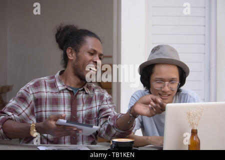Due giovani uomo creativo discutere con laptop e tablet, giovani asiatici e uomo nero lavora con tablet e laptop in un cafe, Papua e uomo asiatico lavorando Foto Stock