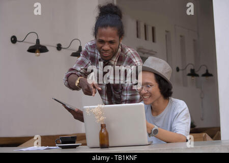 Due giovani uomo creativo discutere con laptop e tablet, giovani asiatici e uomo nero lavora con tablet e laptop in un cafe, Papua e uomo asiatico lavorando Foto Stock