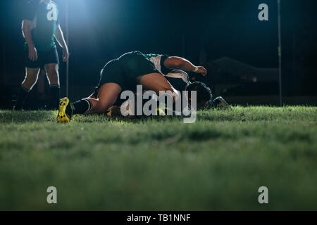 Forti giocatori di rugby che lottano per la palla durante la partita allo stadio. squadra di rugby che cerca di giocare a palla in una partita notturna in un'arena sportiva. Foto Stock