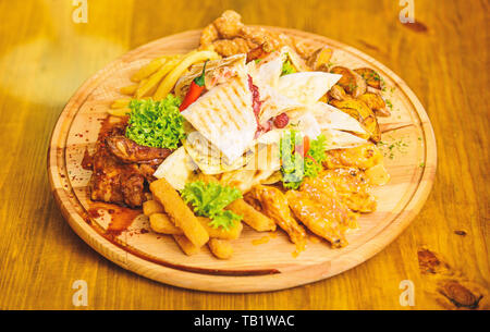 Pub menu snack. Gustosi spuntini deliziosi. Snack per la birra. Il cibo del ristorante. Tavola di legno con un sacco di patatine fritte bastoncini di pesce burrito e bistecca di carne con insalata mista. Ad alto contenuto calorico snack per il gruppo amici. Foto Stock