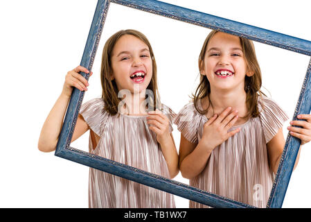 Gemello ragazze stanno rendendo felici espressioni con cornice immagine. Bambini, sorelle, ragazze in posa di studio con Picture Frame, facendo diverse f Foto Stock