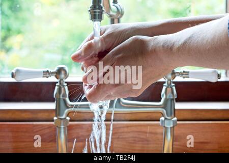 L'uomo lavaggio delle mani sotto i rubinetti ad un lavello da cucina nel Regno Unito. Foto Stock