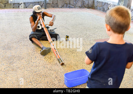 Ragazzo caucasico guardando più in anticipo l'uomo la riproduzione di musica, di Kuranda, Australia Foto Stock