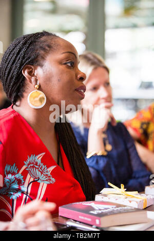 Donna con cornrows indossare orecchini d'oro e rosso top seduti ad un tavolo, in ascolto attento. Foto Stock