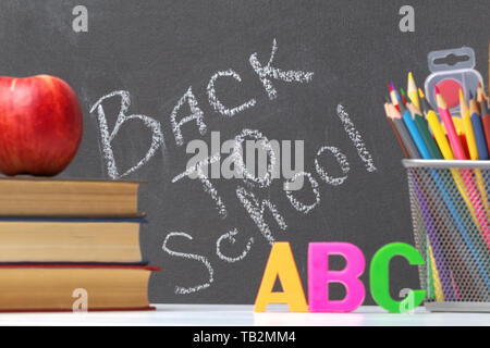 Una pila di libri di testo, un apple, lettere dell'alfabeto A, B, C, matite, pennelli, vernici contro una lavagna nera dello sfondo. Il concetto di educat Foto Stock