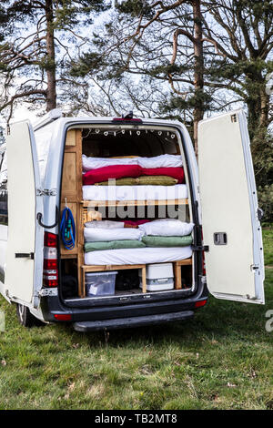 Vista posteriore del camper parcheggiato su un prato, pile di materassi e la biancheria da letto nel retro del veicolo. Foto Stock