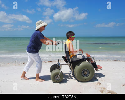 Donna disabile in sedia a rotelle spiaggia gode del sole e sabbia a Honeymoon Island State Park a Dunedin, Florida, Stati Uniti d'America, 10 maggio 2019, © Katharine Andrioti Foto Stock