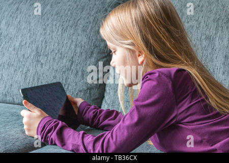 Una ragazza giace sul divano con un tablet PC nelle sue mani Foto Stock