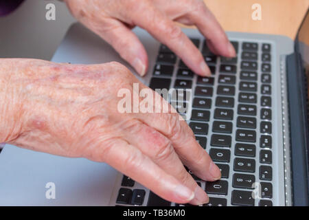 Close-up di un 95-anno-vecchia donna di vecchie mani digitando su una tastiera del notebook Foto Stock