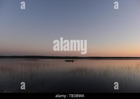 Каyaking persone sulle calme acque del lago nella luce del tramonto di ritorno da una escursione Foto Stock