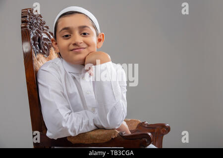 Giovane ragazzo musulmano che indossa il cappuccio seduti sulla sedia e sorridente Foto Stock