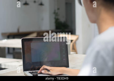 Vista posteriore studente facendo compiti a casa con il computer portatile e la scrittura in notebook presso il cafe, giovane uomo che lavora presso il cafe con notebook e laptop Foto Stock