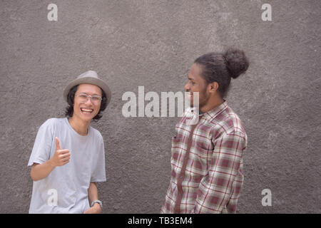 Due migliori amici di azione e ridere ogni altro uomo asiatico e uomo nero amico che pongono in telecamera Foto Stock