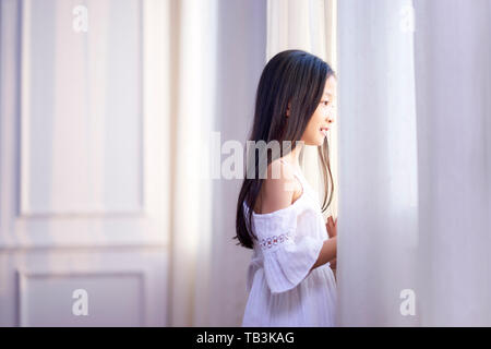 Bella ragazza asiatica con lunghi capelli neri guardando fuori della finestra in camera da letto Foto Stock