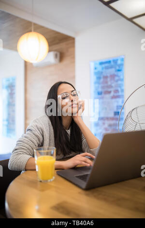 Ritratto di donna aucasian utilizzando laptop a tavola in cucina mentre interna avente la colazione a casa Foto Stock