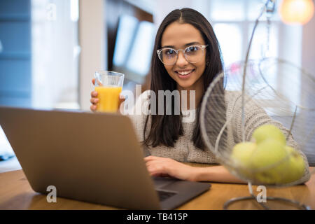 Ritratto di bella donna caucasica utilizzando laptop a tavola in cucina mentre interna avente la colazione a casa Foto Stock