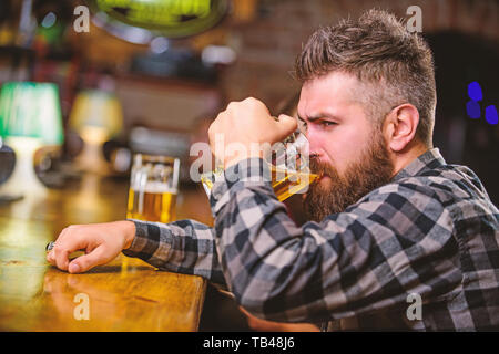 Ordine di bere alcol. Il bar è un luogo rilassante hanno bere e rilassarsi. Hipster rilassante presso il bar con birra. Uomo con barba trascorrere il tempo libero nella barra di colore scuro. Brutale parigamba uomo barbuto sedersi al banco bar bere birra. Foto Stock