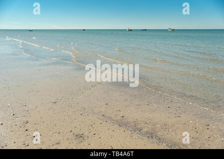 Una bellissima spiaggia di sabbia soffice e mare blu onda. panorama del paesaggio marino con cielo blu a luce diurna. barche da pesca sul orizzonte Foto Stock