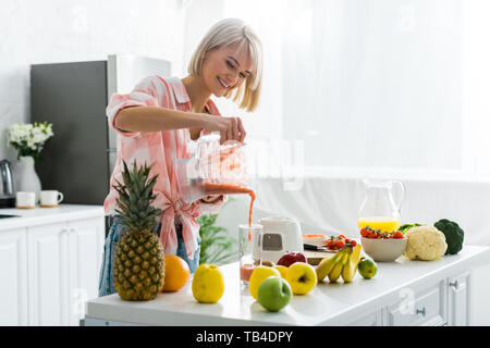 Allegro giovane donna versando frullato gustoso in vetro Foto Stock