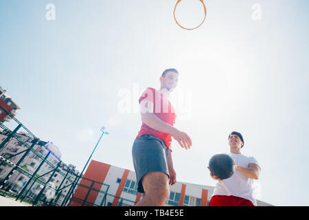 Due amici caucasici indossando rosso dell'apparecchiatura di sport giocando basketballs all'aperto in una giornata di sole mentre essi dribbling e spingere l'altra. Foto Stock