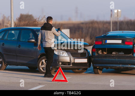 Un uomo con un telefono intelligente per scattare una foto dei danni alla sua vettura provocato da un incidente di macchina Foto Stock