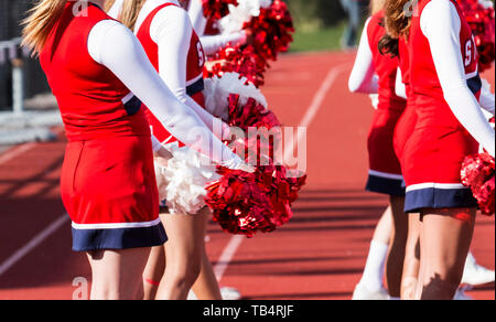 High school cheerleaders hanno i loro pompon davanti a loro mentre si guarda la partita di calcio in attesa di allegria. Foto Stock