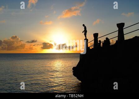 Un uomo si erge sulla cima di un bordo di battuta pronta a tuffarsi a Taga beach, Tinian, al tramonto Foto Stock