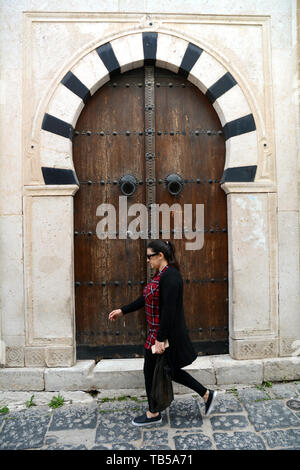 Un tunisino donna cammina oltre la tradizionale in legno chiodati porta di una casa del XVI secolo in un vicolo della medina (città vecchia) di Tunisi, Tunisia. Foto Stock