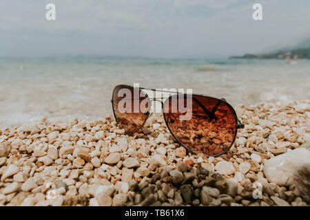 Occhiali da sole sulla spiaggia in estate. Colore marrone occhiali da sole  con gocce di acqua di mare riflettente e pietre Foto stock - Alamy