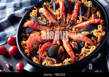 Tradizionali fatti in casa Fideua spagnola, un noodle Paella con frutti di mare - gamberoni, bianco carne di pesce, calamari, cozze in una padella nera su una tabella di calcestruzzo Foto Stock