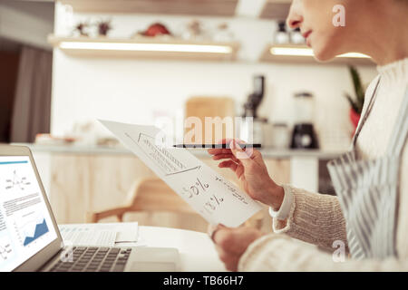 Lo sviluppo del business. Concentrato di smart business donna seduta al tavolo con il suo computer portatile e alcuni fogli di carta a lavorare sullo sviluppo della sua ca Foto Stock