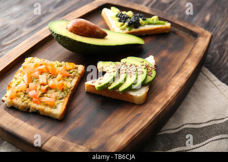 Scheda con gustosi panini avocado su un tavolo di legno Foto Stock