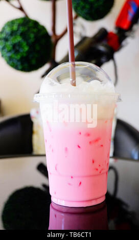 Fragola Rosa latte shake / rosa ghiacciata di latte fresco in una tazza di plastica e paglia sul tavolo coffee shop Foto Stock