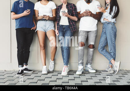 Sempre connesso persone su telefoni cellulari moderni. Un gruppo di ragazzi che usano telefoni cellulari all'aperto, spazio libero Foto Stock