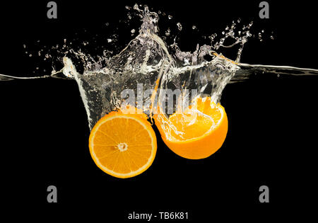 Fresh cut arance caduti in acqua con splash, sfondo nero Foto Stock