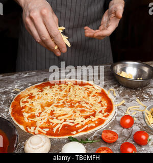 Cucina Italiana. Cuocere la mano l'aggiunta di formaggio grattugiato per la pizza in pizzeria Foto Stock